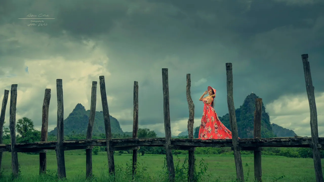 High-fashion editorial portrait in red dress under dramatic storm clouds, by Htoo Wai